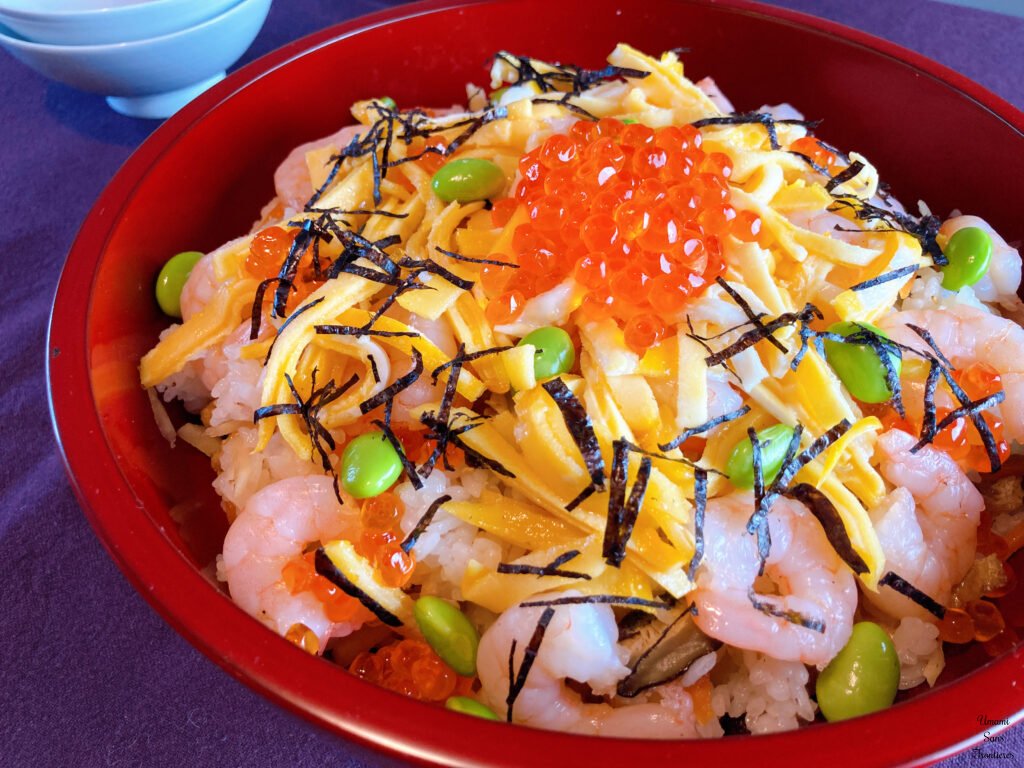Chirashi sushi garnished inure shrimps edamame nori knish tamale